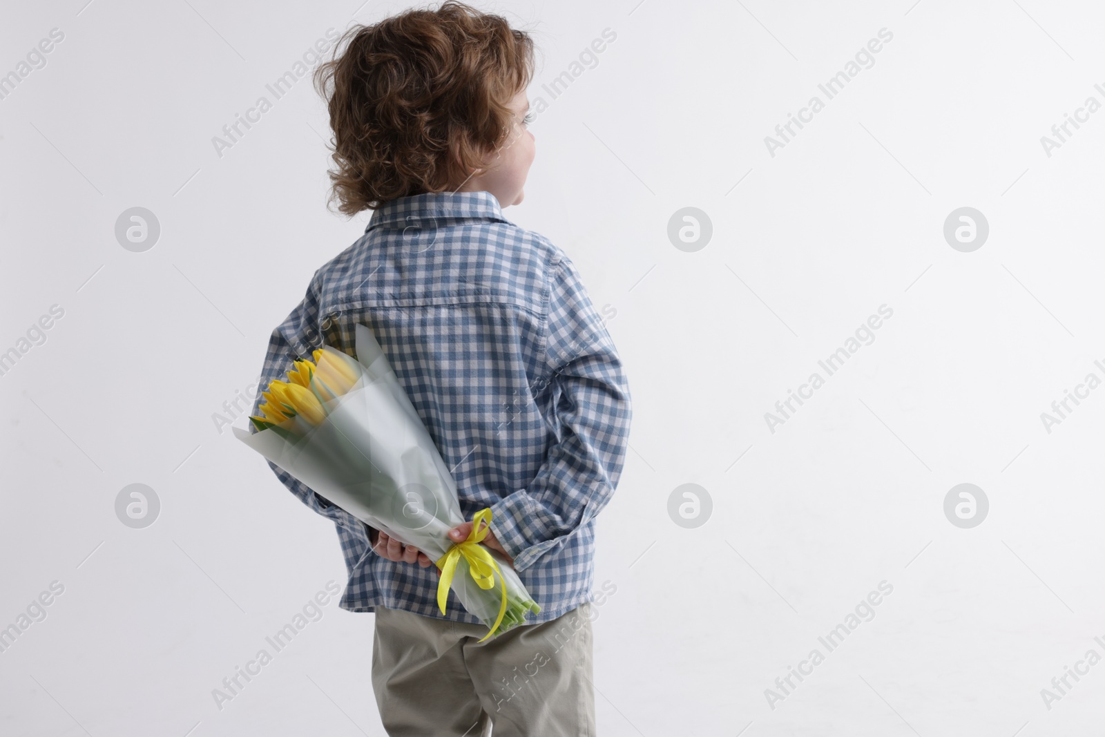 Photo of Little boy with bouquet of tulips behind his back on white background. Space for text