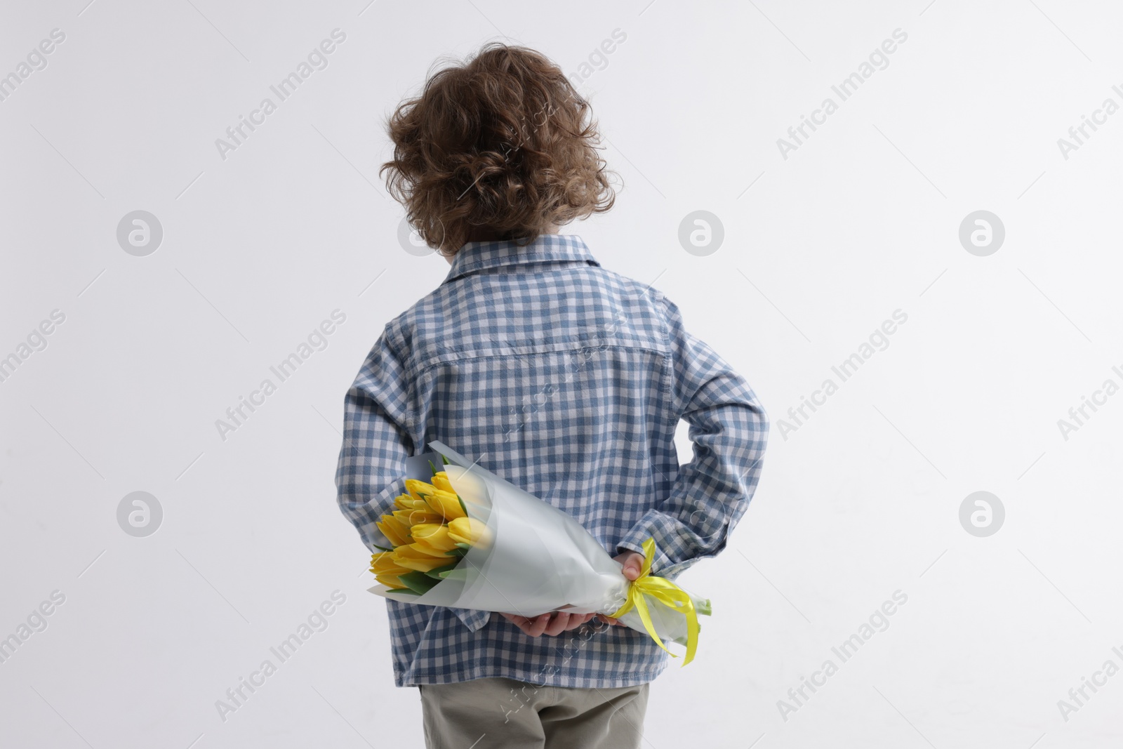 Photo of Little boy with bouquet of tulips behind his back on white background