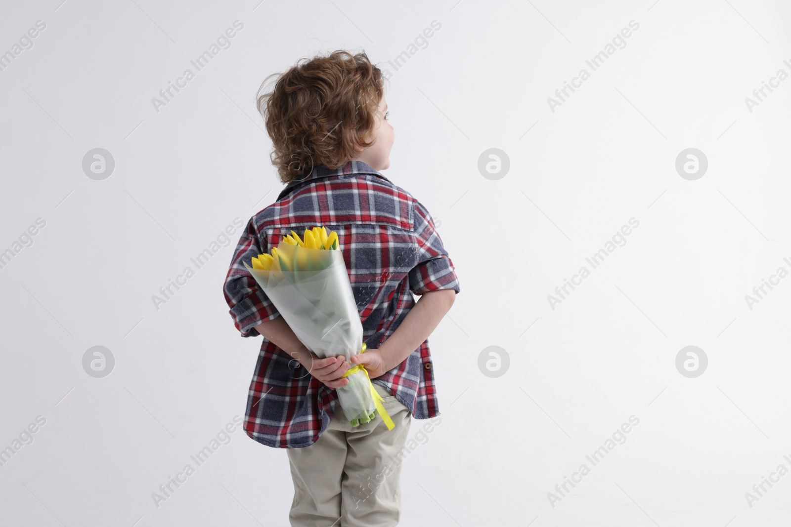 Photo of Little boy with bouquet of tulips behind his back on white background