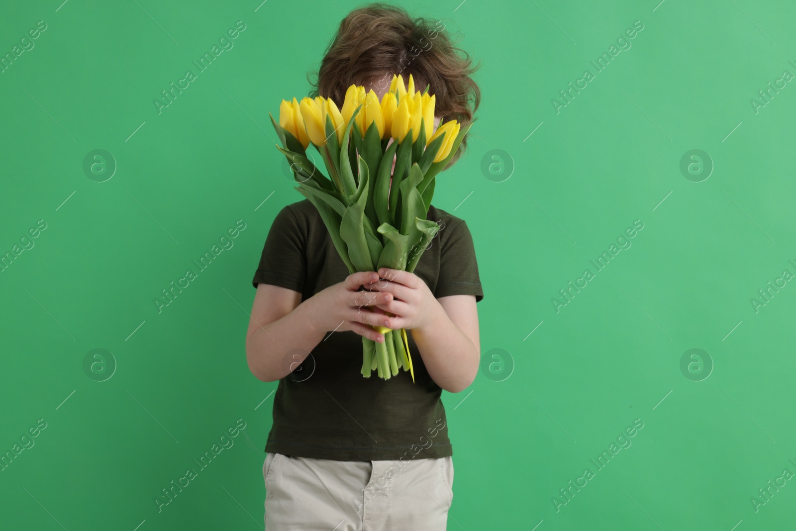 Photo of Little boy hiding behind bouquet of tulips on green background