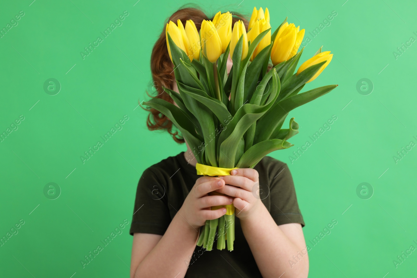 Photo of Little boy hiding behind bouquet of tulips on green background