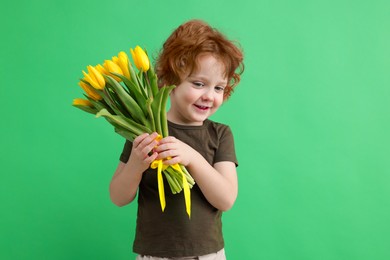 Photo of Cute little boy with bouquet of tulips on green background