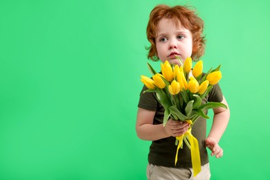 Photo of Cute little boy with bouquet of tulips on green background. Space for text