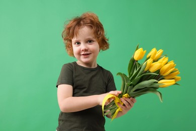 Photo of Cute little boy with bouquet of tulips on green background