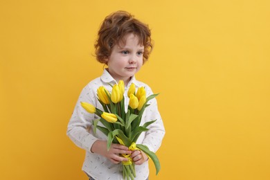 Photo of Cute little boy with bouquet of tulips on yellow background