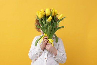 Little boy hiding behind bouquet of tulips on yellow background