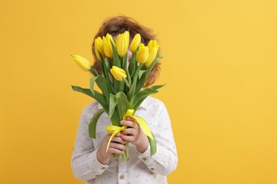 Photo of Little boy hiding behind bouquet of tulips on yellow background