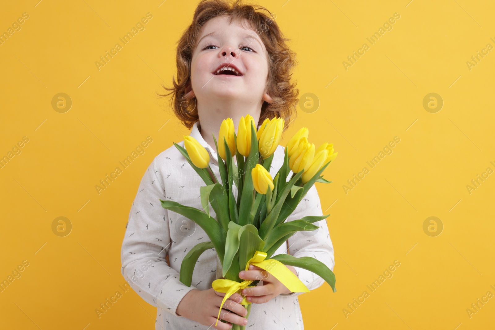 Photo of Cute little boy with bouquet of tulips on yellow background