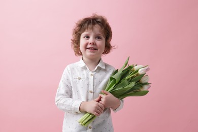 Photo of Cute little boy with bouquet of tulips on light pink background