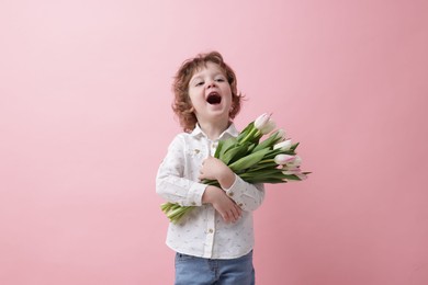 Cute little boy with bouquet of tulips on light pink background