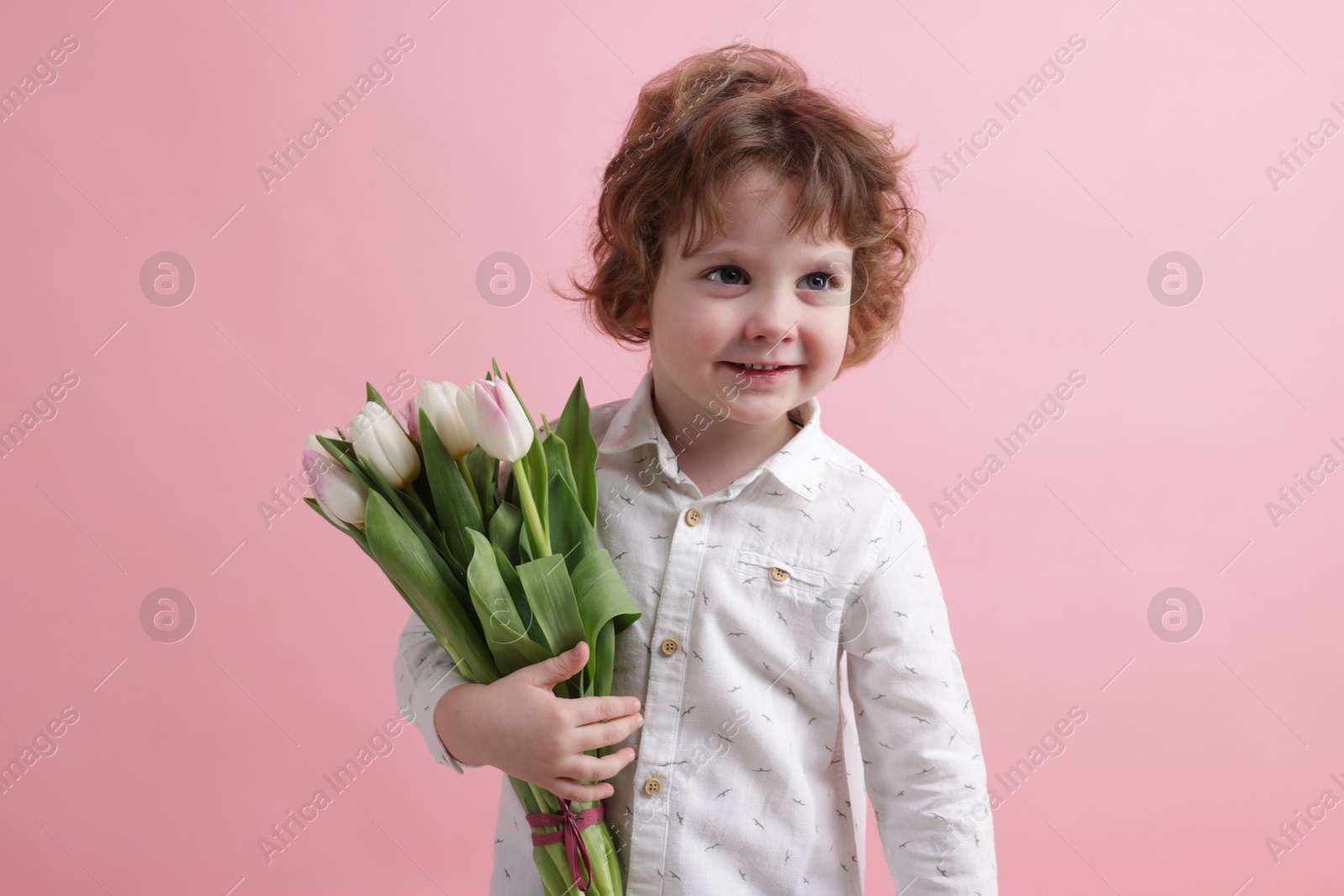 Photo of Cute little boy with bouquet of tulips on light pink background