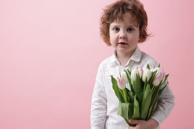 Cute little boy with bouquet of tulips on light pink background. Space for text