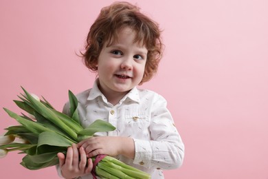 Photo of Cute little boy with bouquet of tulips on light pink background