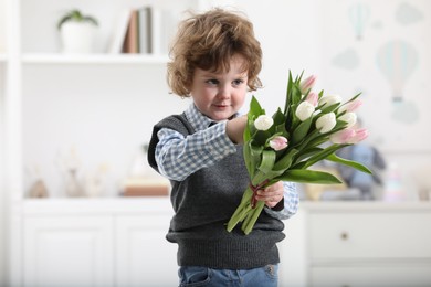 Photo of Cute little boy with bouquet of tulips at home