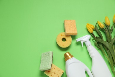 Photo of Spring cleaning. Detergents, sponges and tulips on green background, flat lay. Space for text