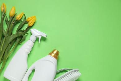 Photo of Spring cleaning. Detergents, brush and tulips on green background, flat lay. Space for text