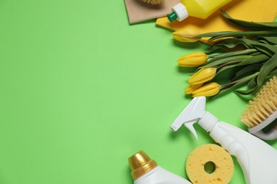 Photo of Spring cleaning. Detergents, supplies and tulips on green background, flat lay. Space for text