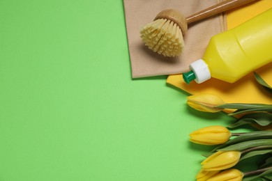 Photo of Spring cleaning. Detergent, supplies and tulips on green background, flat lay. Space for text