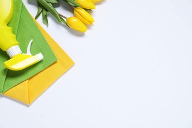 Photo of Spring cleaning. Detergent, rags and tulips on white background, flat lay. Space for text