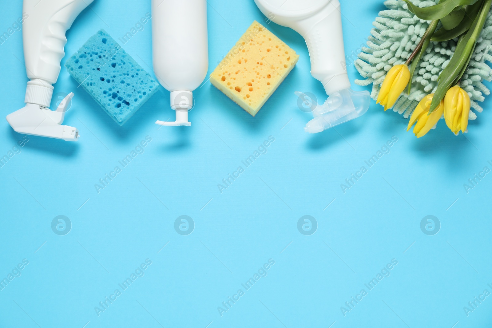 Photo of Spring cleaning. Detergents, supplies and tulips on light blue background, flat lay. Space for text