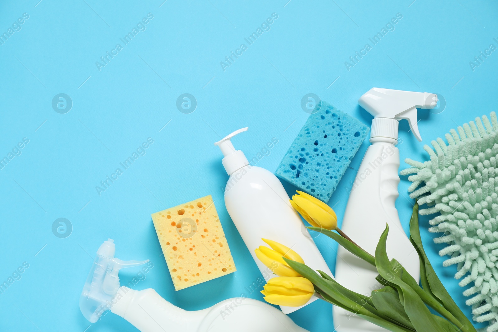 Photo of Spring cleaning. Detergents, supplies and tulips on light blue background, flat lay. Space for text