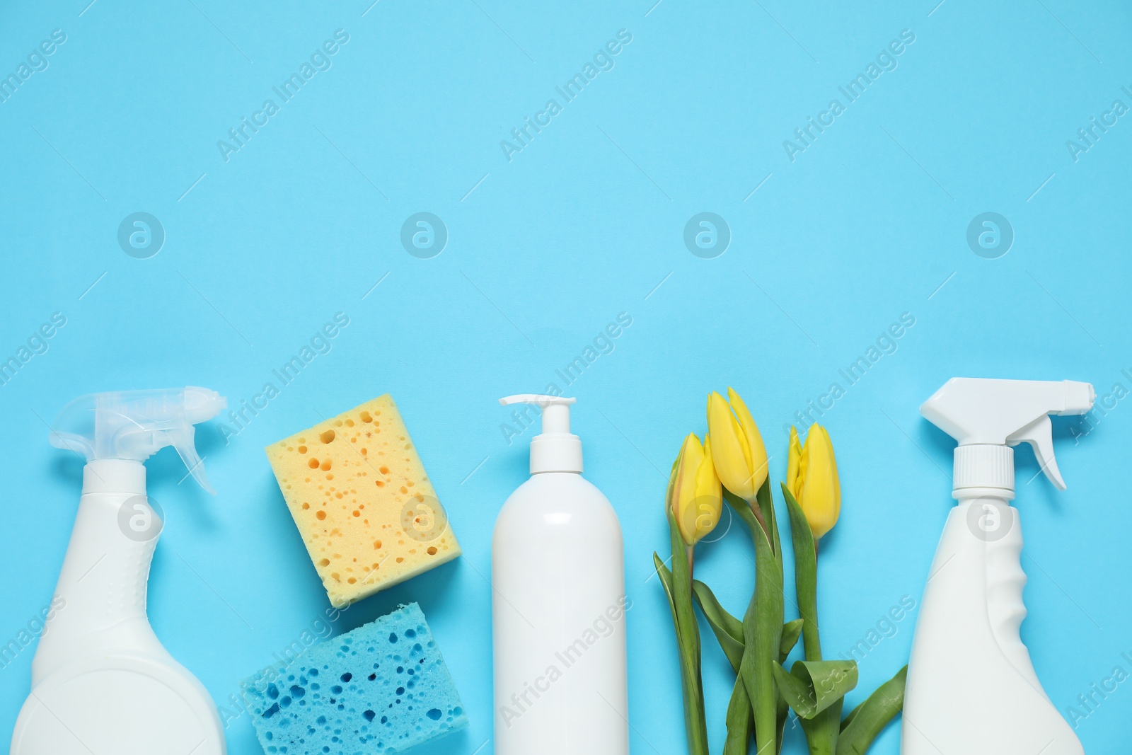 Photo of Spring cleaning. Detergents, supplies and tulips on light blue background, flat lay. Space for text