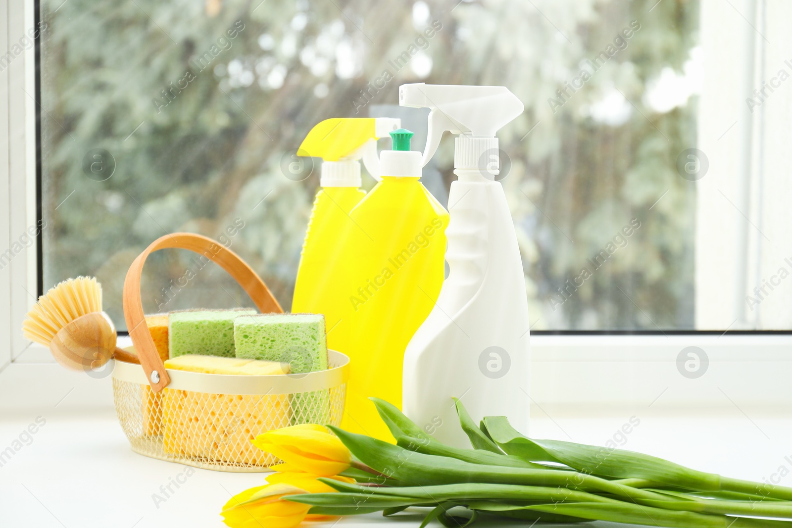 Photo of Spring cleaning. Detergents, supplies and tulips on windowsill indoors