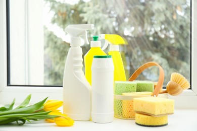 Photo of Spring cleaning. Detergents, supplies and tulips on windowsill indoors