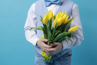 Photo of Little boy with bouquet of tulips on light blue background, closeup