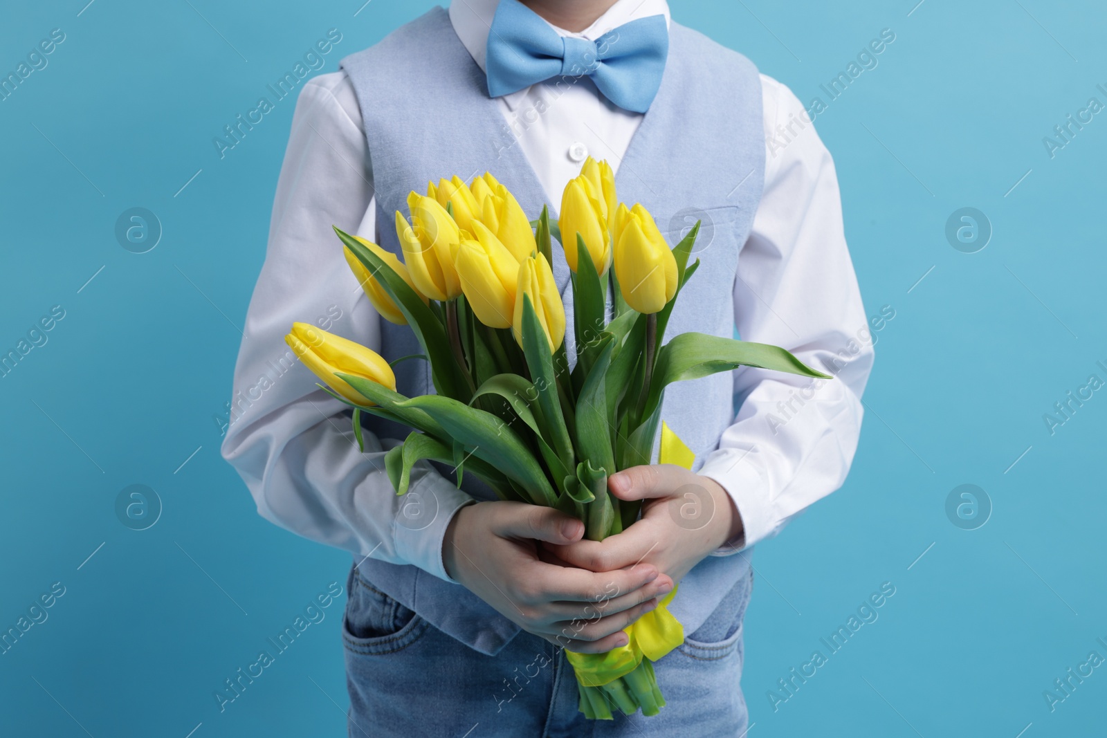 Photo of Little boy with bouquet of tulips on light blue background, closeup