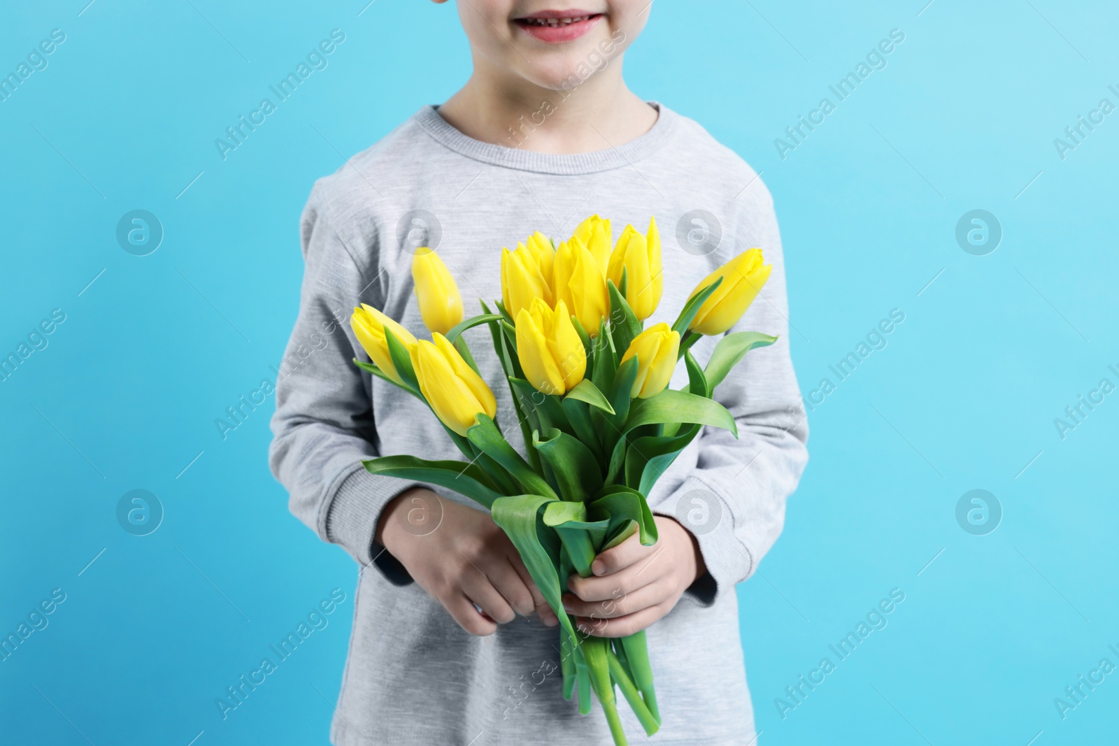 Photo of Little boy with bouquet of tulips on light blue background, closeup