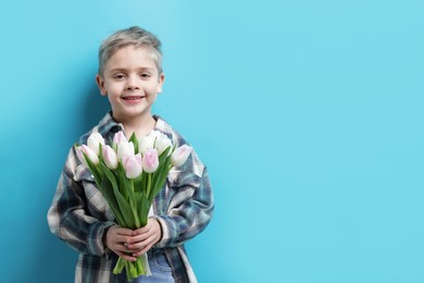 Photo of Cute little boy with bouquet of tulips on light blue background. Space for text