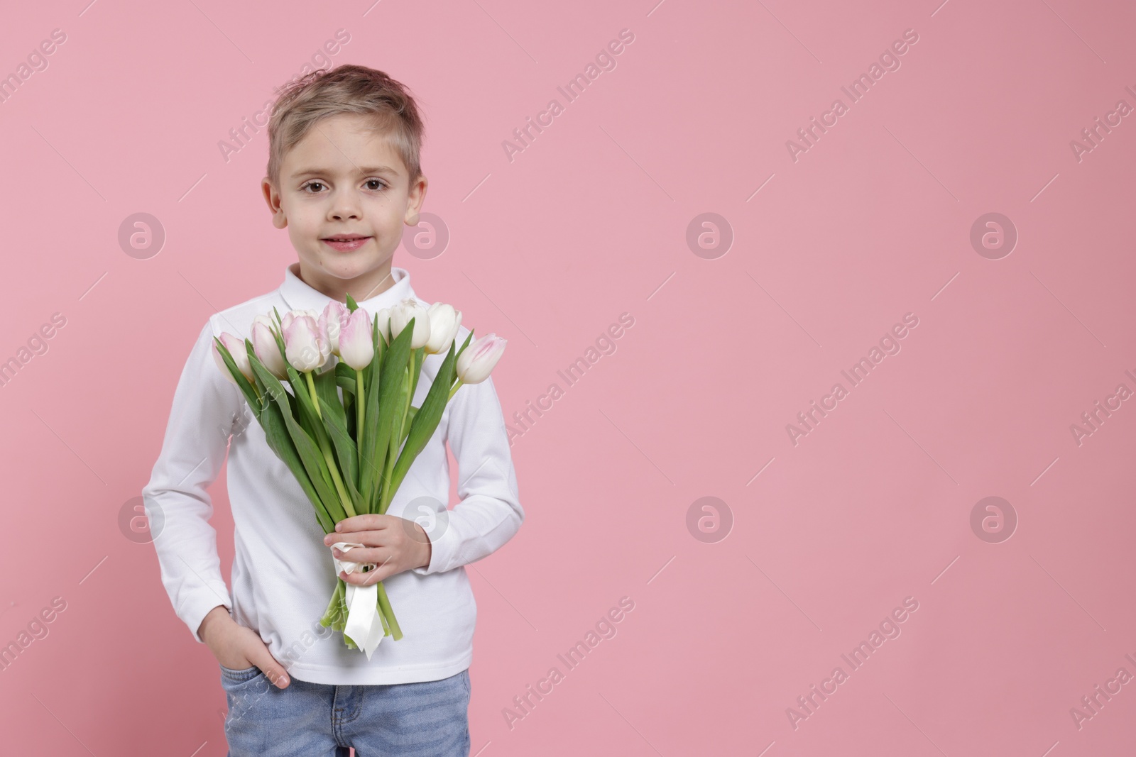 Photo of Cute little boy with bouquet of tulips on light pink background. Space for text