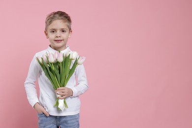 Cute little boy with bouquet of tulips on light pink background. Space for text