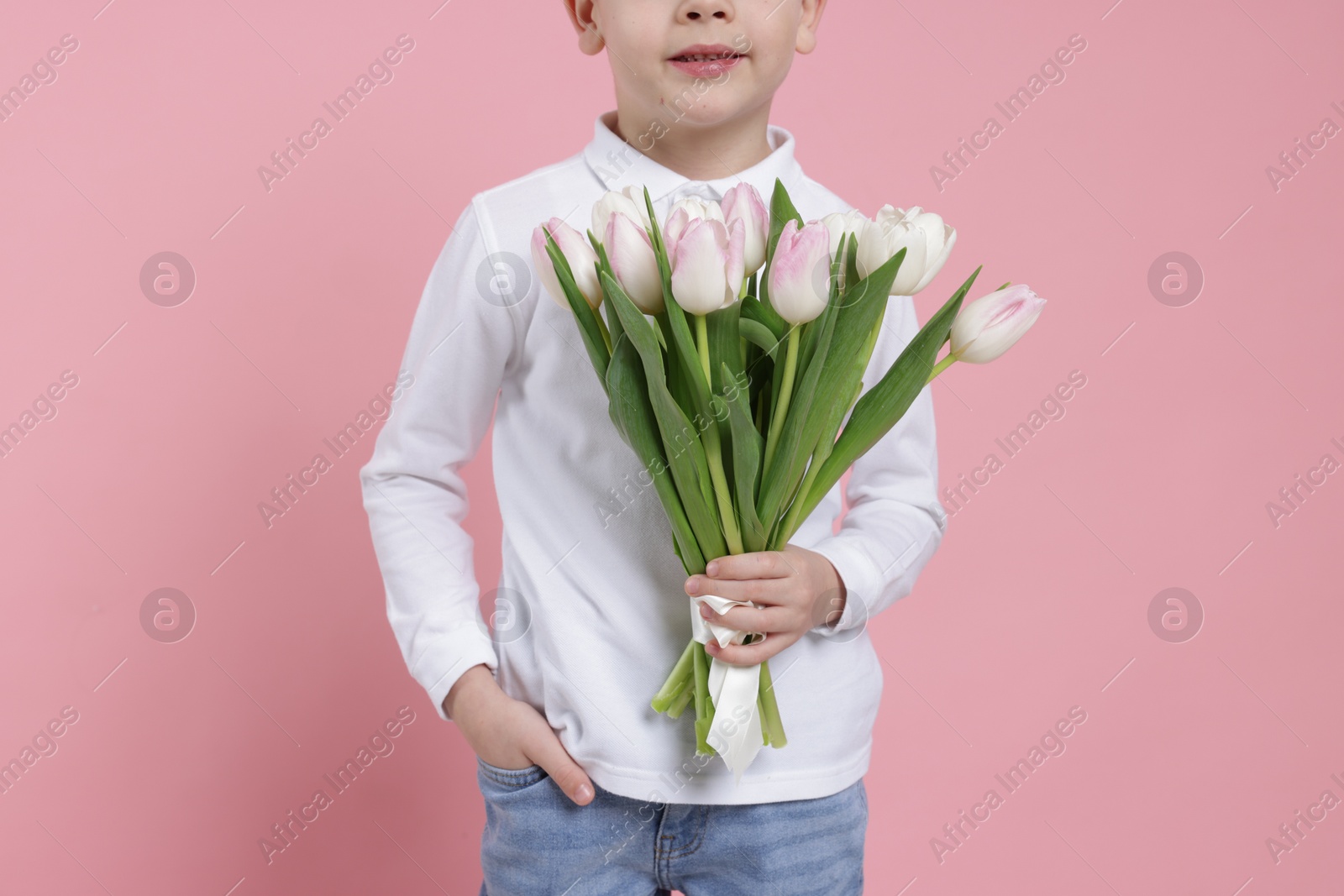 Photo of Little boy with bouquet of tulips on light pink background, closeup