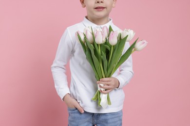 Photo of Little boy with bouquet of tulips on light pink background, closeup