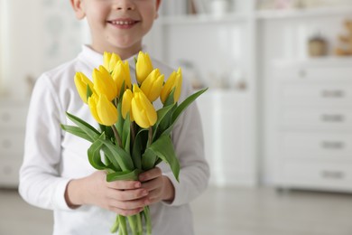 Photo of Little boy with bouquet of tulips at home, closeup