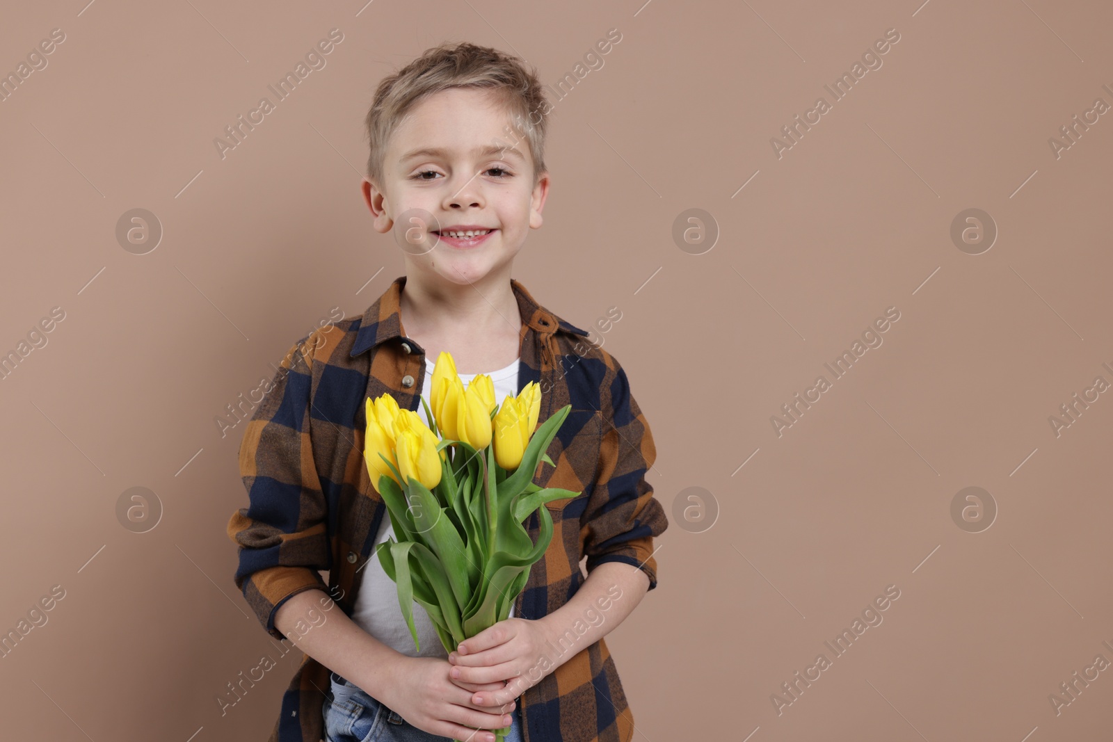 Photo of Cute little boy with bouquet of tulips on brown background. Space for text