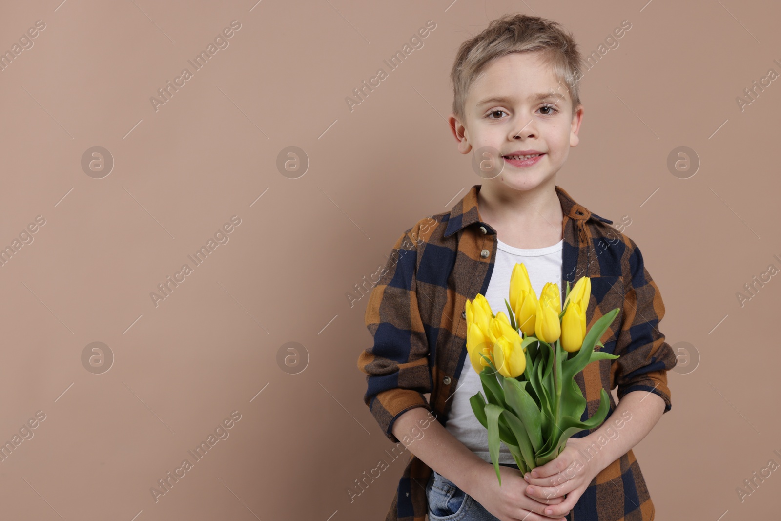 Photo of Cute little boy with bouquet of tulips on brown background. Space for text