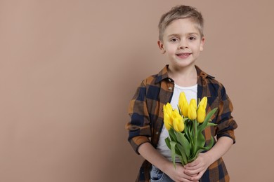 Cute little boy with bouquet of tulips on brown background. Space for text