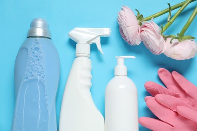 Photo of Spring cleaning. Detergents, gloves and flowers on light blue background, flat lay