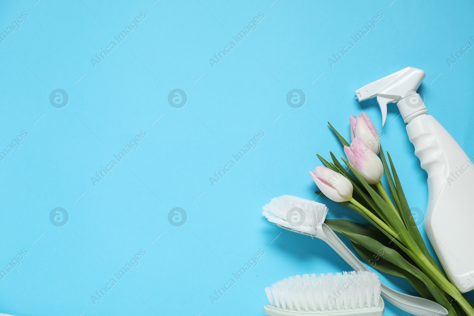 Photo of Spring cleaning. Detergent, brushes and tulips on light blue background, flat lay. Space for text