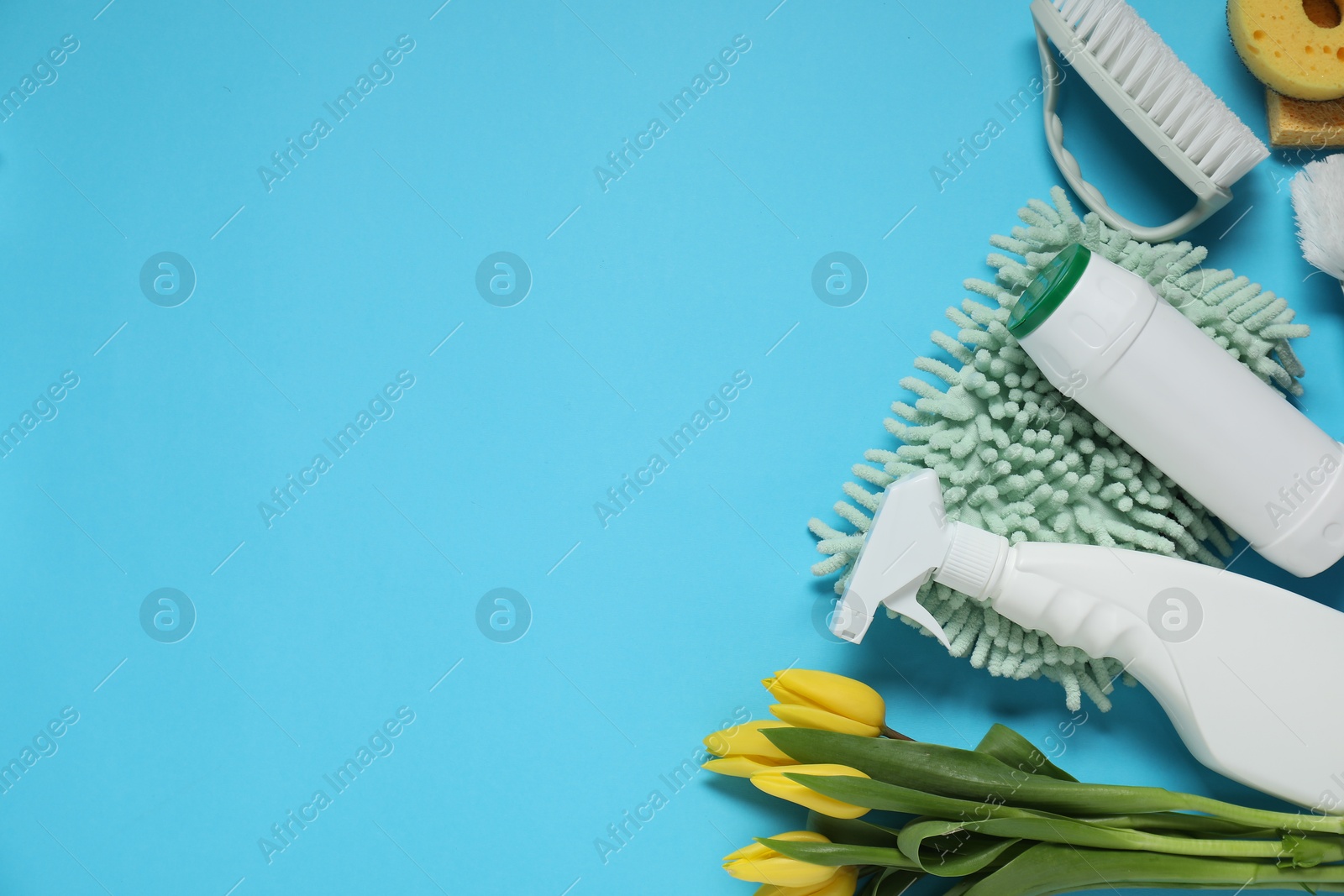 Photo of Spring cleaning. Detergents, supplies and tulips on light blue background, flat lay. Space for text