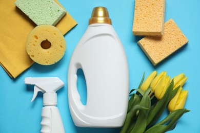 Photo of Spring cleaning. Detergents, supplies and tulips on light blue background, flat lay