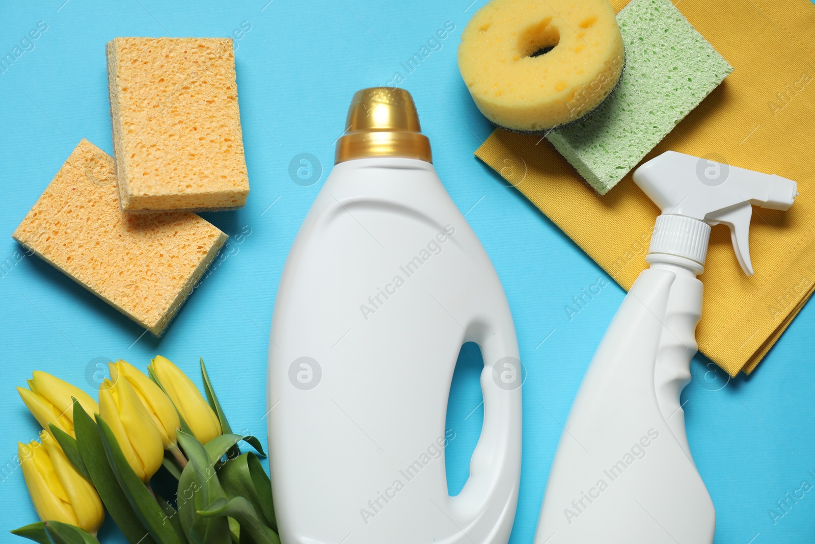 Photo of Spring cleaning. Detergents, supplies and tulips on light blue background, flat lay