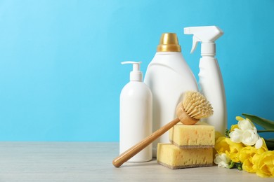 Photo of Spring cleaning. Detergents, supplies and flowers on wooden table against light blue background, space for text