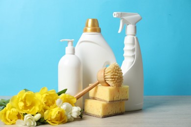 Photo of Spring cleaning. Detergents, supplies and flowers on white wooden table against light blue background