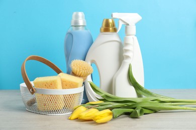 Photo of Spring cleaning. Detergents, supplies and tulips on white wooden table against light blue background