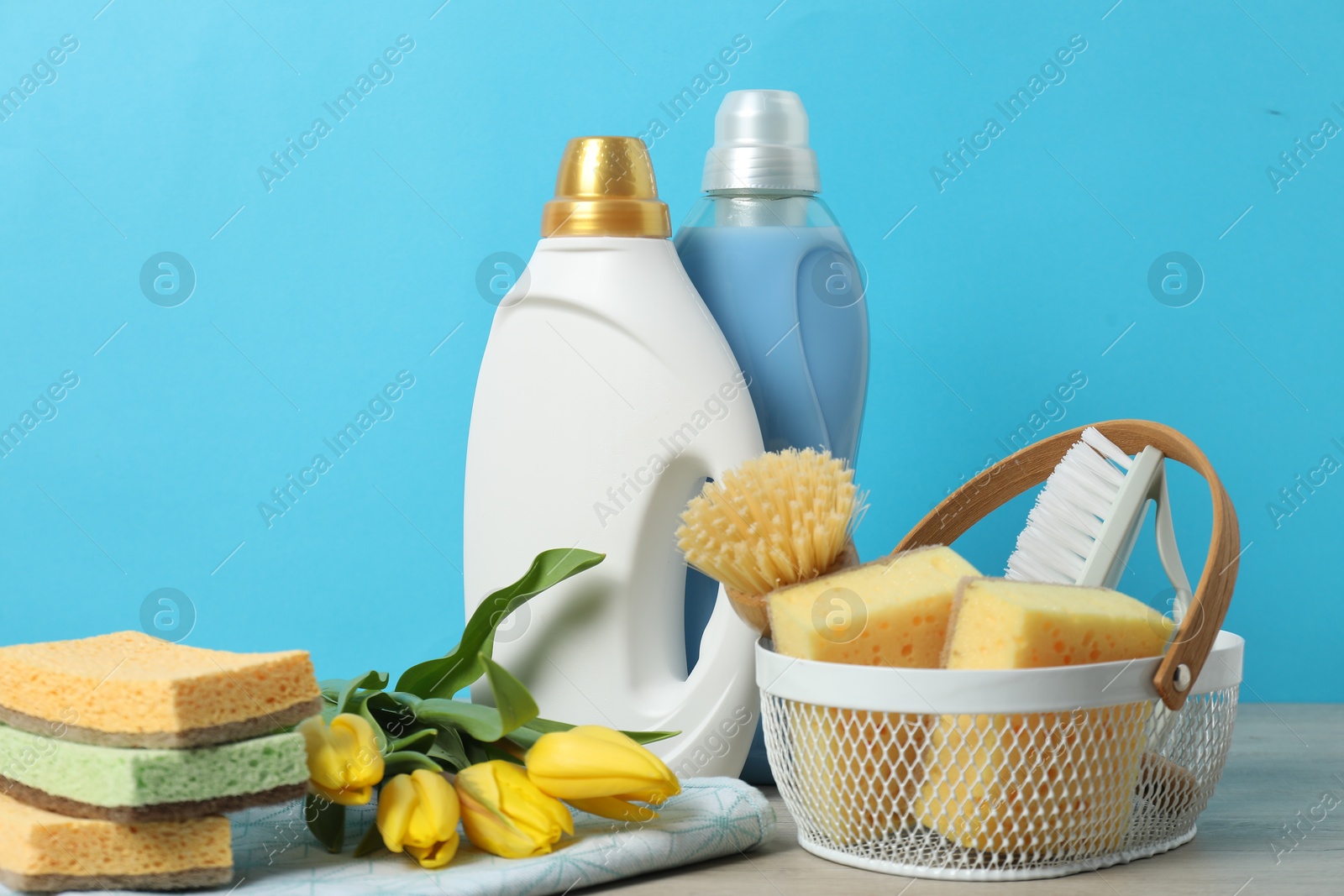 Photo of Spring cleaning. Detergents, supplies and tulips on white wooden table against light blue background