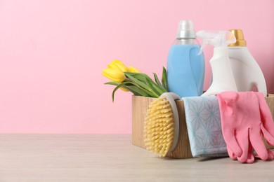 Photo of Spring cleaning. Detergents, supplies and tulips on white wooden table against pink background, space for text